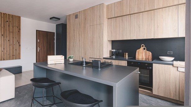 A modern kitchen with wooden cabinets, a central island with bar stools, a black countertop, and a built-in oven. - Humo Idealna Lokalizacja Centrum Gara (Poznan)