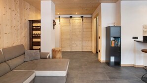 A modern interior with a sectional sofa, a wooden wall, a bookshelf, and a door with a sliding mechanism. - Apartment 'Camino' with Mountain View and Wi-Fi (Santa Caterina)