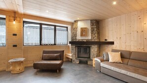 A cozy living room with a stone fireplace, wooden walls, and a brown leather sofa. - Apartment 'Camino' with Mountain View and Wi-Fi (Santa Caterina)