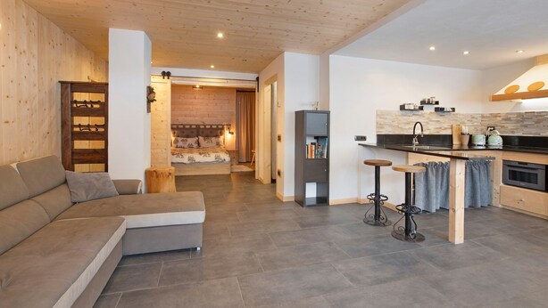 A modern living area with a sofa, a kitchen with a stove, and a dining area with stools. - Apartment 'Camino' with Mountain View and Wi-Fi (Santa Caterina)