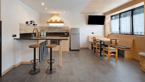 A modern kitchen with a dining area, wooden furniture, and a TV mounted on the wall. - Apartment 'Camino' with Mountain View and Wi-Fi (Santa Caterina)