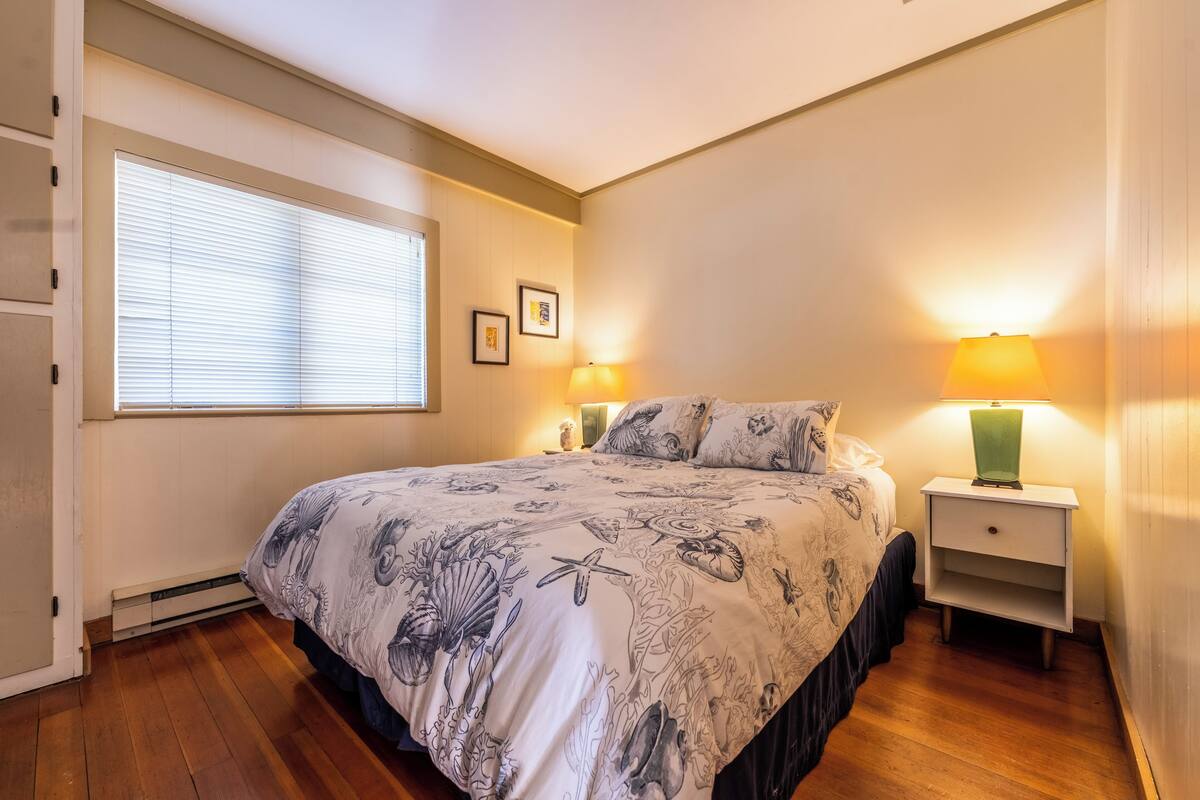 Une chambre à coucher avec un grand lit, deux lampes de chevet, une fenêtre avec des stores et un tableau encadré au mur.