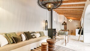 Een woonkamer met een bank, houten bijzettafeltjes, een kamerkleed met patroon en een hanglamp.