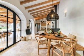 A dining area with a round wooden table, wicker chairs, and a large arched window. - Villa 'Las Brisas' with Mountain View, Wi-Fi and Air Conditioning (Jávea)