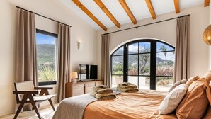 Een slaapkamer met een groot bed, een televisie, een bureau en een stoel, met uitzicht op een bergachtig landschap.