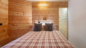 A wooden-paneled room with a bed, two pillows with deer head designs, a wall-mounted light, and a small picture.