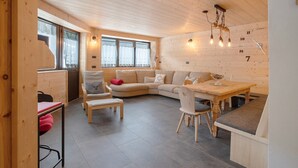 A cozy room with a wooden ceiling, a curved sofa, a dining table, and a small kitchen area.