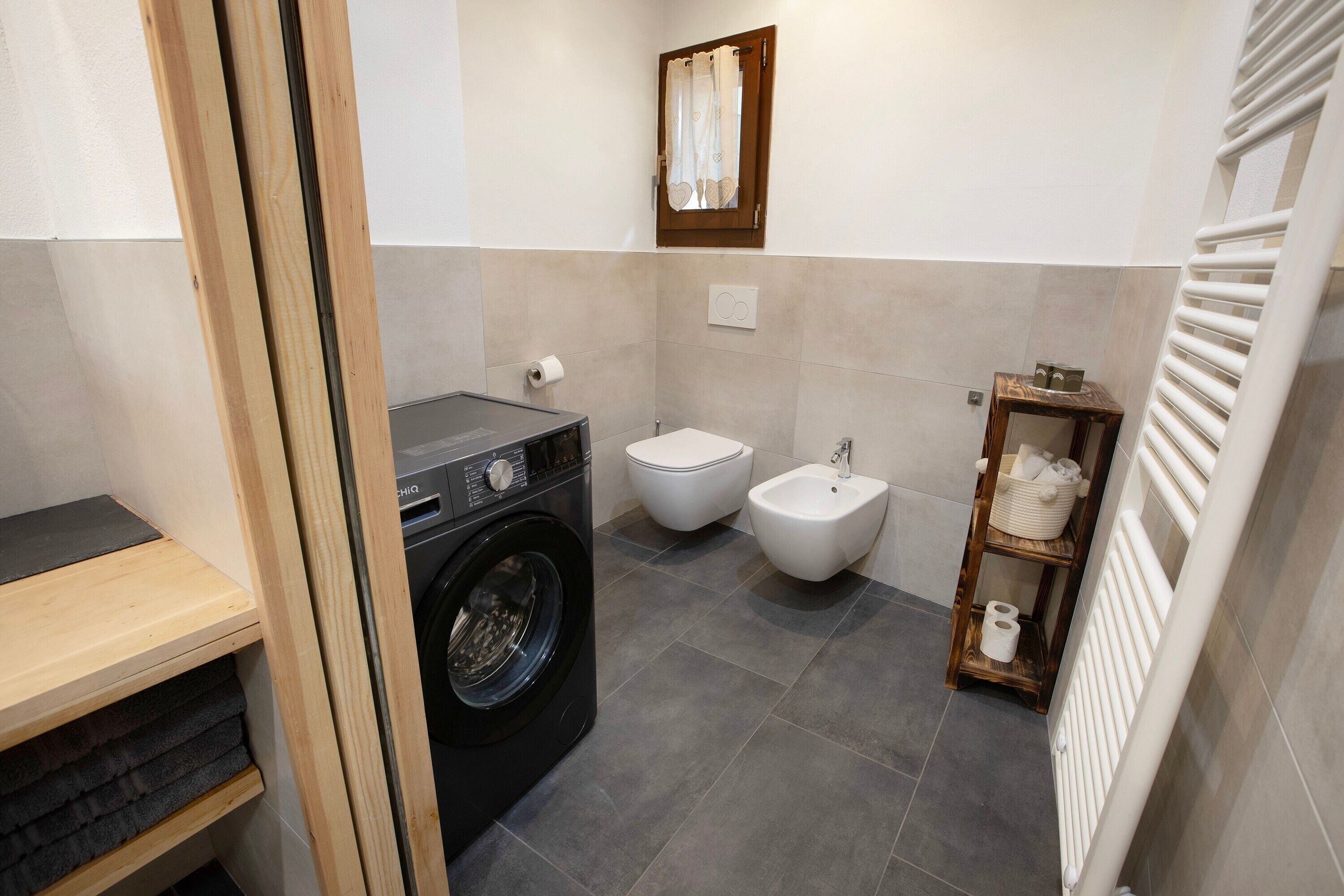 Une petite salle de bain équipée d’un lave-linge, de toilettes, d’un bidet et d’une petite étagère où sont rangées les serviettes.