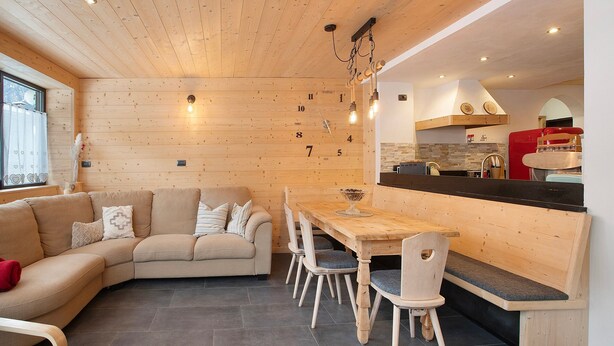 A cozy interior with a wooden ceiling, a dining area with a bench, and a kitchen visible through an archway.