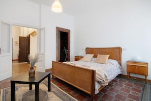 A bedroom with a wooden bed, bedside tables, a nightstand, a rug, and a door leading to another room.