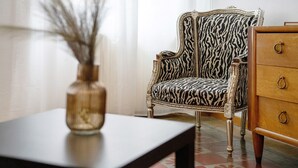 A room with a zebra-patterned chair, a wooden dresser, and a vase with branches.