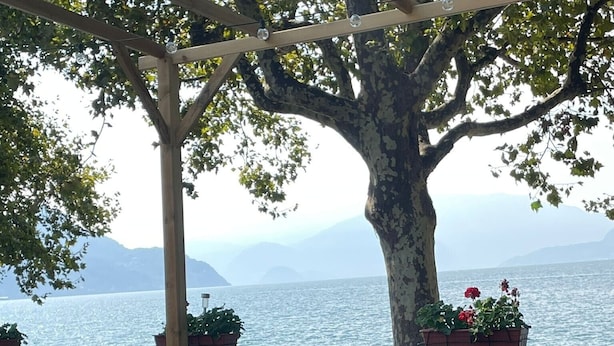 An outdoor seating area with tables and chairs, potted plants, and a view of the sea.