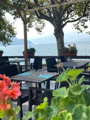 An outdoor seating area with tables and chairs, potted plants, and a view of the sea. - Apartment 'Francesco' 1of4 of Villa Paruzzi 6 Min To Lake Como (Dervio)