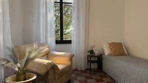 A room with a sofa, a small table with a plant, a window with curtains, and a checkered floor.