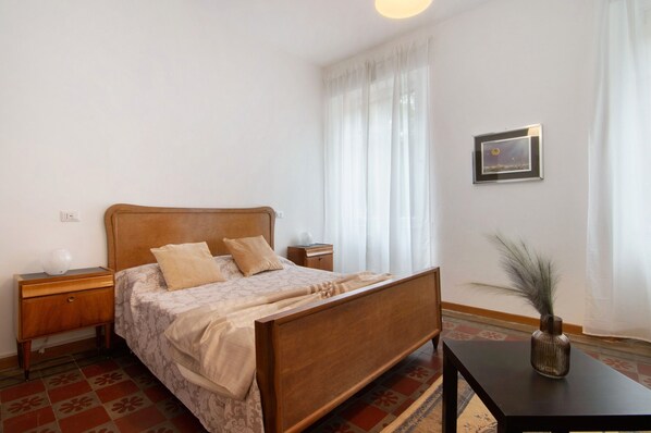 A bedroom with a wooden bed, a nightstand, a bedside table, a framed picture on the wall, and a vase on a table. - Apartment 'Francesco' 1of4 of Villa Paruzzi 6 Min To Lake Como (Dervio)