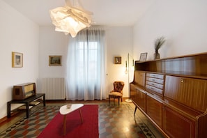 A room with a radiator, a vintage radio, a red rug, a wooden cabinet, and a chair.