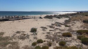 Una playa con un paseo marítimo de madera que conduce a la orilla, dunas de arena y una vista despejada del océano.