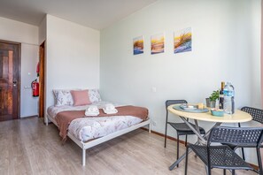 A bedroom with a bed, a table with chairs, a fire extinguisher, and wall art. - Gaivotas House Apartment with Balcony and Wi-Fi Access (Alvor)