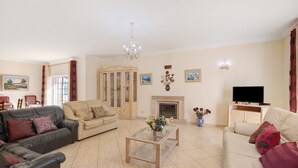Ein Wohnzimmer mit Glastisch, Sofas, Fernseher, Kamin und einer Kristallleuchter.
