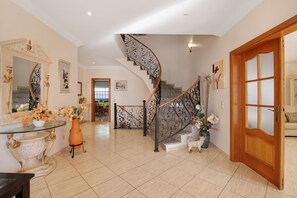 Un vestíbulo espacioso con una imponente escalera, una mesa de centro de cristal y un jarrón decorativo.