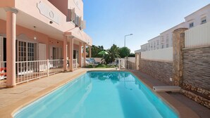Ein Swimmingpool mit weißem Zaun, einem überdachten Sitzbereich und einem Gebäude mit rosafarbener Fassade.