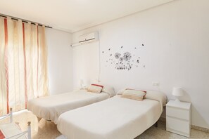 Ein Zimmer mit zwei Betten, einem Nachttisch, einer Lampe, einer Klimaanlage und einer Wanddekoration.