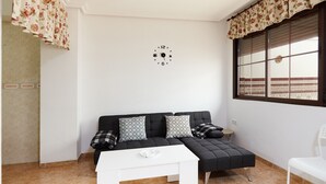A modern room with a black sofa, a white table, and a window with blinds.