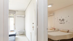A hotel room with two beds, a small table, a chair, and a wall-mounted air conditioner.