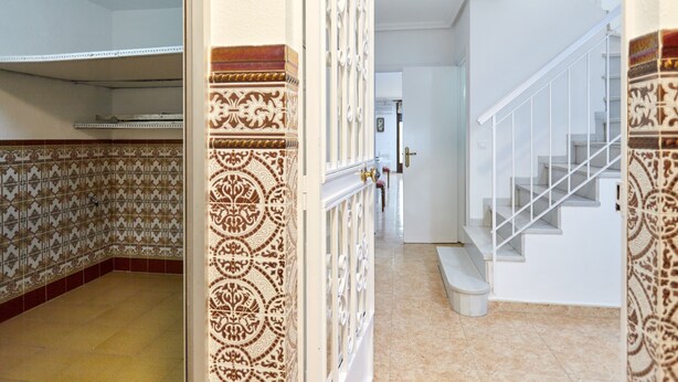 A hallway with patterned walls, a staircase with white railings, and a door at the end.