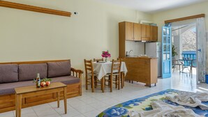 A room with a sofa, a dining table with chairs, a kitchen area, and a view through an open door.