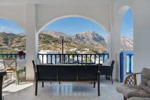 Un espace extérieur aménagé, abrité et doté de mobilier en osier, d’une table et de chaises, offrant une vue sur un paysage montagneux.