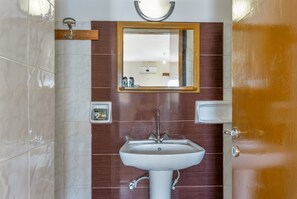 Une salle de bain avec un lavabo blanc, un miroir encadré en bois et une porte dotée d’une poignée en laiton.
