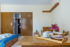 Quarto com cama, mesa de madeira com bandeja, cadeira, pequena mesa com um vaso de flores e guarda-roupa de madeira.