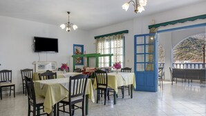 A dining area with tables and chairs, a TV mounted on the wall, and a view through an open door. - Apartment 'No 2' with Sea View, Wi-Fi and Air Conditioning (Karpathos)
