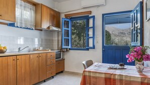 A kitchen with wooden cabinets, a sink, and a window with blue shutters. - Apartment 'No 2' with Sea View, Wi-Fi and Air Conditioning (Karpathos)