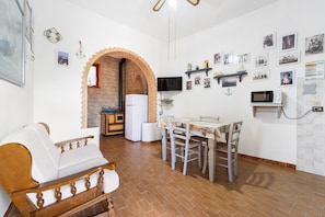 A kitchen with a dining table, chairs, a sofa, a TV, and a brick wall.
