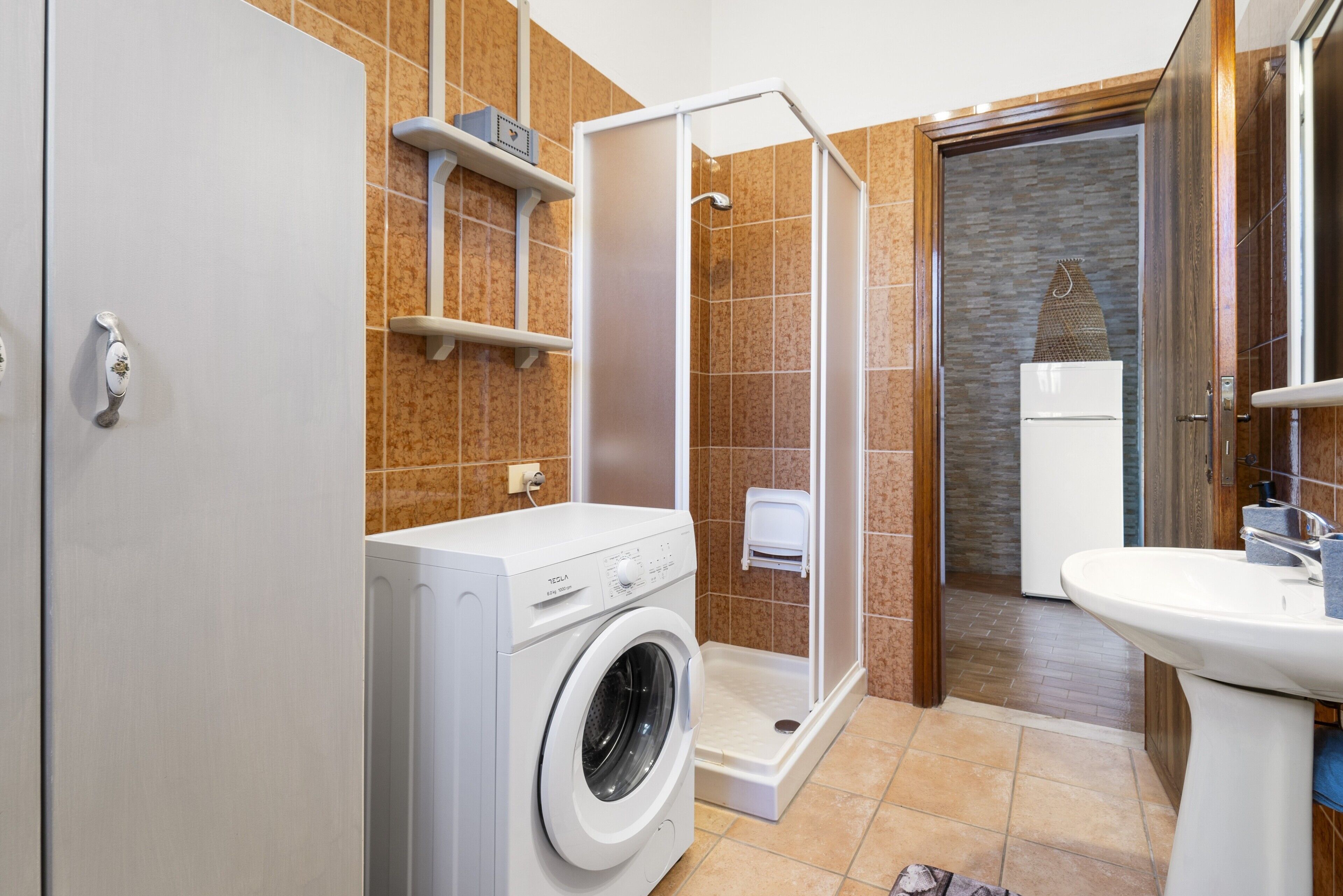 A modern bathroom with a washing machine, a shower enclosure, and a sink.