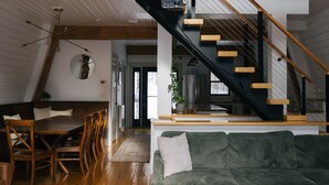 A spacious loft with a wooden staircase, a dining area, and a green sofa.
