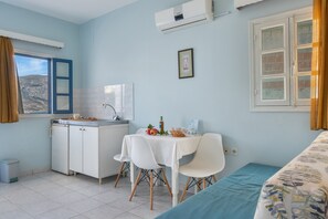 Une pièce comprenant un lit, une petite kitchenette, une table à manger avec des chaises, une fenêtre avec des rideaux et un tableau au mur.