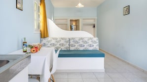 A room with a bed, a table with a bottle and fruit, a window with curtains, and a hanging light fixture.