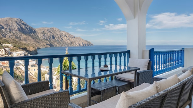 A balcony with wicker furniture, a table, and a view of the sea and mountains.