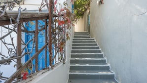 A staircase leading up to a building with a blue door, surrounded by white walls and some vegetation.