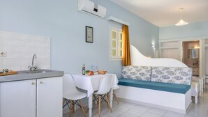 A compact room with a kitchenette, a dining area, and a bed with a blue and white floral bedspread.