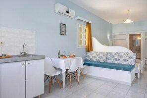 Een compacte kamer met een kitchenette, een eethoek en een bed met een bloemenbedekking in blauw en wit.