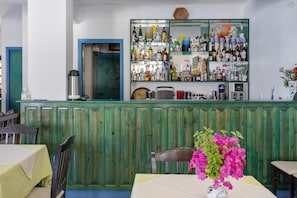 Een bargedeelte met een groene houten toonbank, diverse flessen en een tafel met een bloevas.