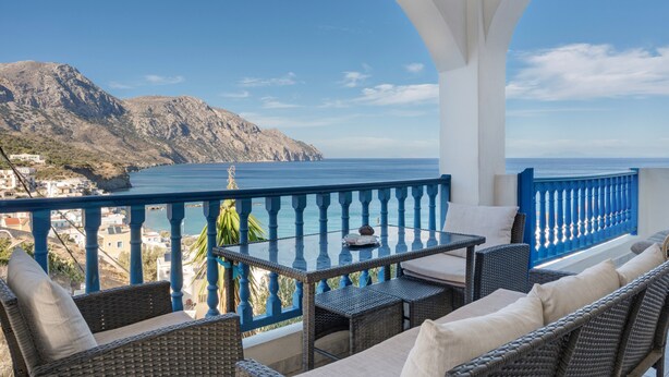 A balcony with wicker furniture, a table, and a view of the sea and mountains. - Apartment 'No 1' with Sea View, Wi-Fi and Air Conditioning (Karpathos)