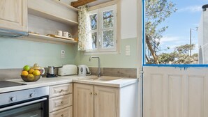 A kitchen with a built-in oven, a sink, and a window with a view of trees. - Apartment 'No 1' with Sea View, Wi-Fi and Air Conditioning (Karpathos)