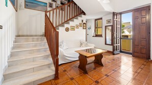 Una escalera conduce a una sala de estar con un sofá, una mesa de ajedrez y una puerta al exterior.