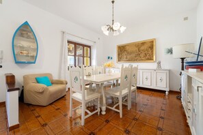 Ein Essbereich mit einem weißen Tisch und Stühlen, einem beigen Sofa, einem dekorativen Regal und einem Bild an der Wand.