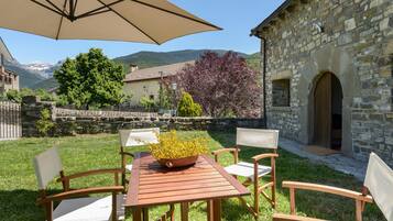Une terrasse extérieure avec une table et des chaises, un bâtiment en pierre et une vue sur les montagnes.